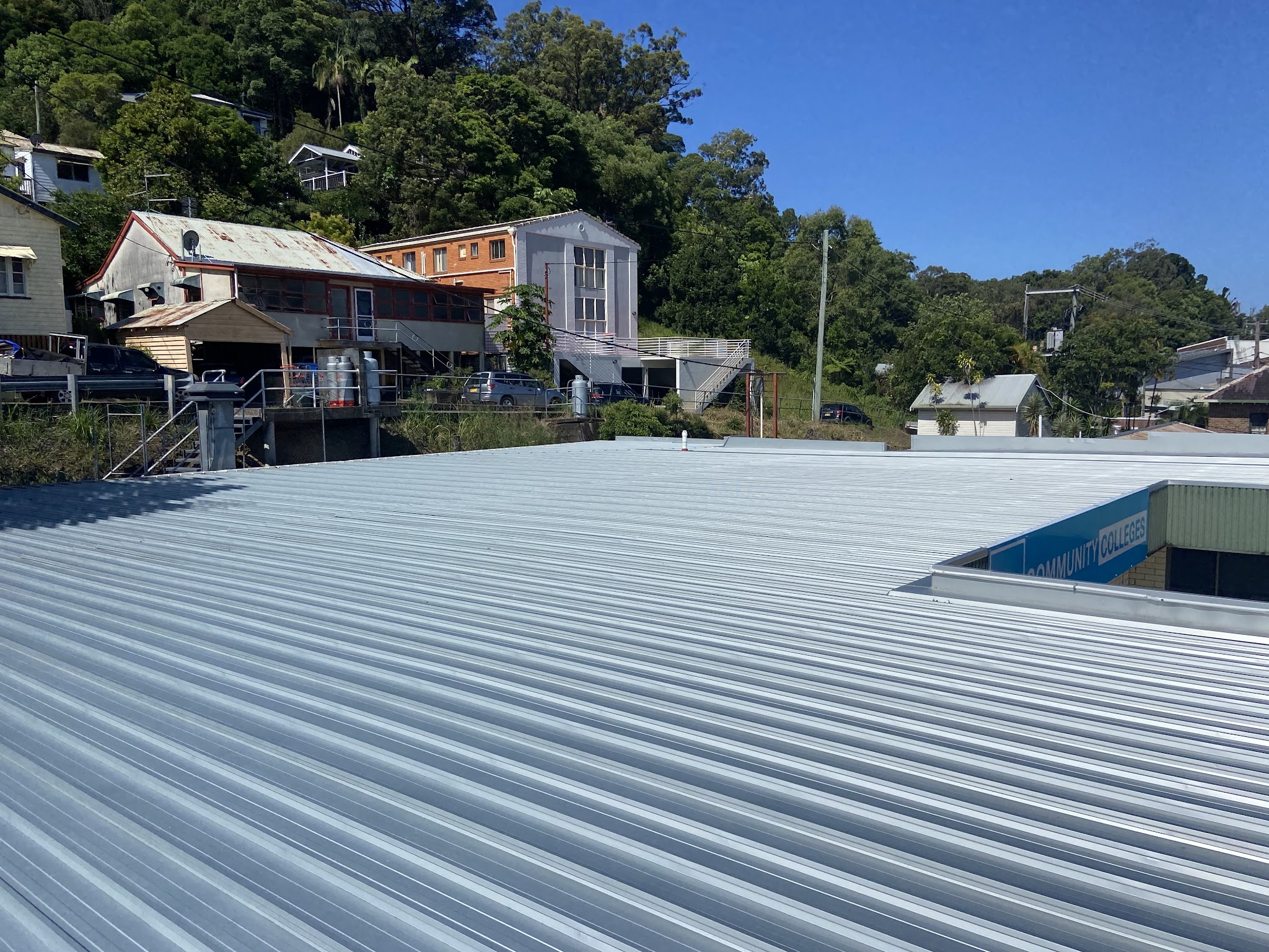 A large new commercial roof in Murwillumbah, with hillside houses and a building sign behind