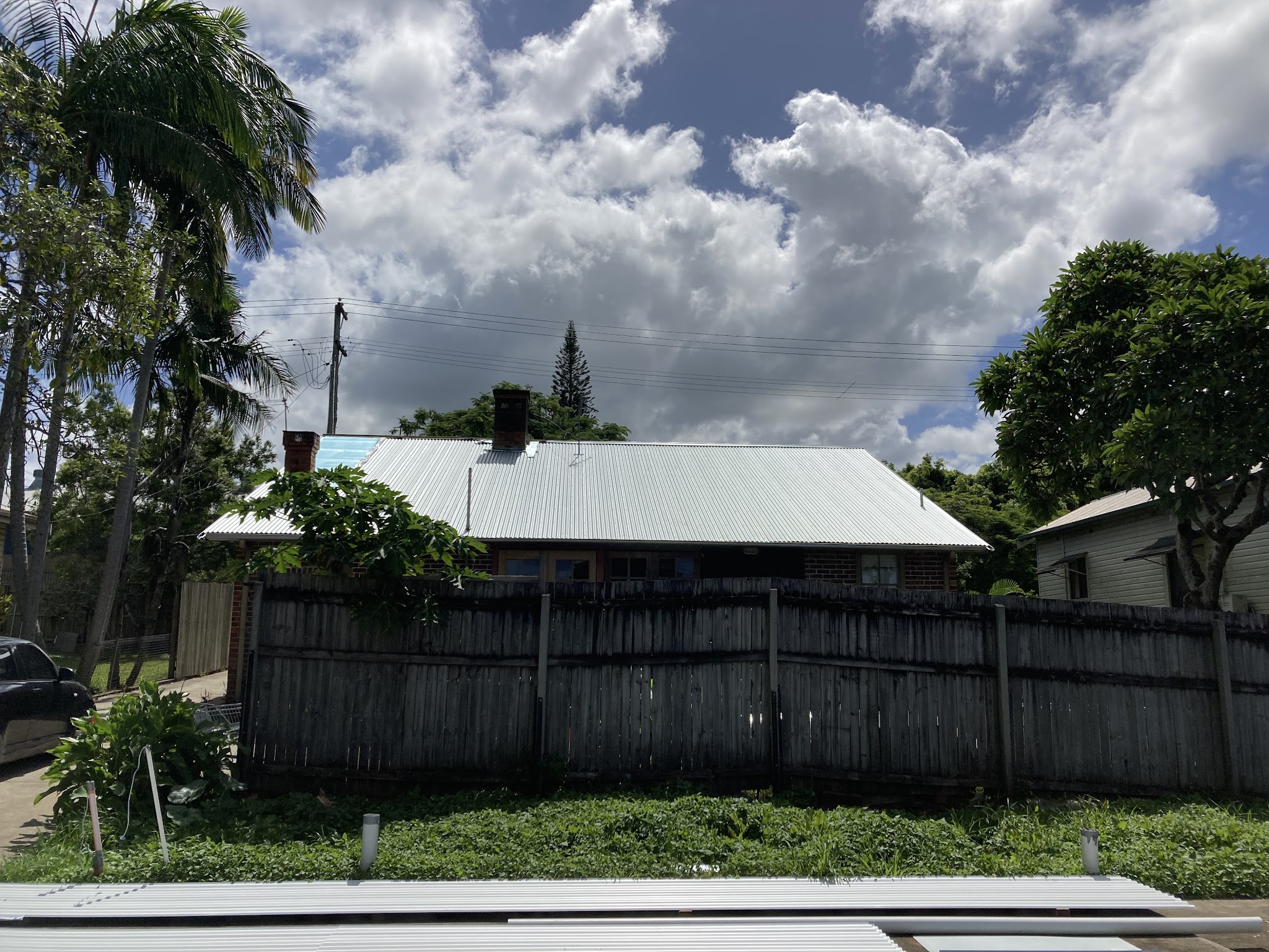 A cottage with a brand new white corrugated roof, fresh sheets stacked in the foreground