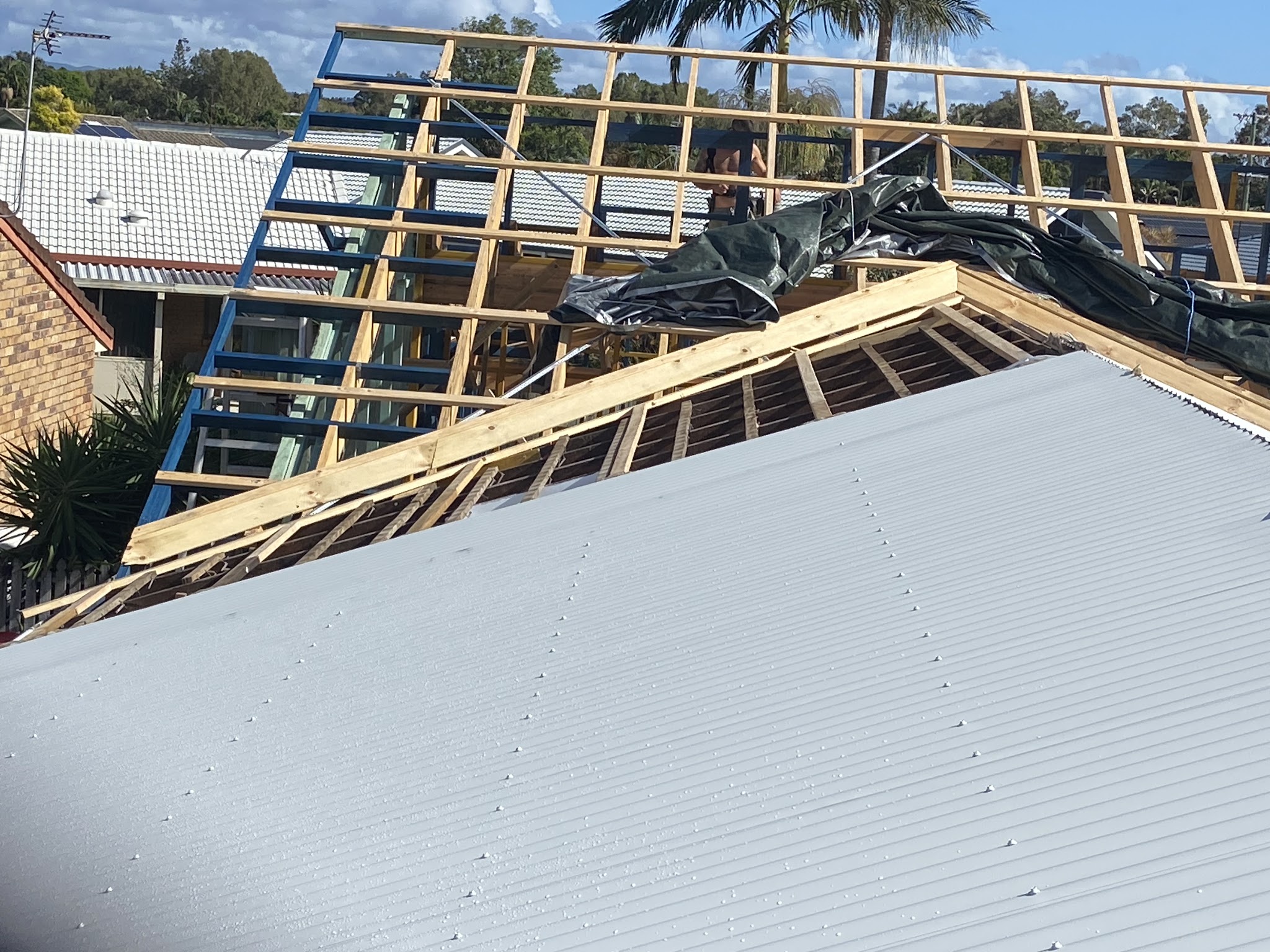 A roof half re-sheeted, with new metal laid on one plane and open timber battens on the other